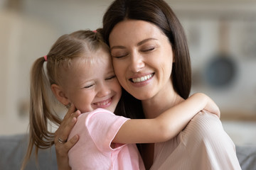 Caring smiling foster mother embrace cute adopted daughter at home