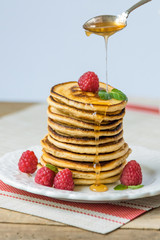 Pancakes with honey and raspberries on a white plate on a wooden table, close up