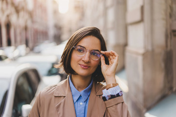 Portrait of Young cheerful business woman in glasses looking at camera while crossing road on daytime