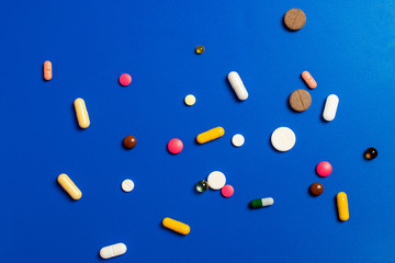 Close-up of assorted multi-colored pills on a blue background. Medical flat lay.