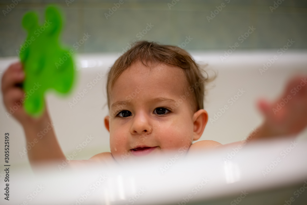 Wall mural Cute Caucasian baby gets out of the bath with a green toy in his hand. close-up, soft focus