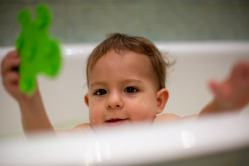 Cute Caucasian baby gets out of the bath with a green toy in his hand. close-up, soft focus