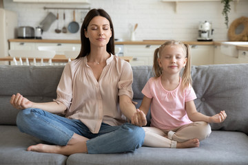 Healthy mom and kid daughter doing yoga exercise on sofa