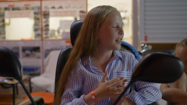 Cute happy girl sitting and talking with friend outdoors. Close-up view of adorable cheerful child with long hair wearing striped shirt and talking in the evening
