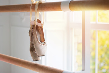 old pointes hang on ballet loom. concept of training and winner, hard work. Pink Ballet shoes at bar in ballet class near big window. Copy space. - Powered by Adobe