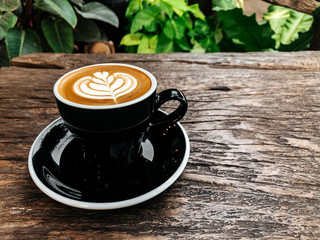 Latte art coffee placed in red ceramics mug and wooden table.