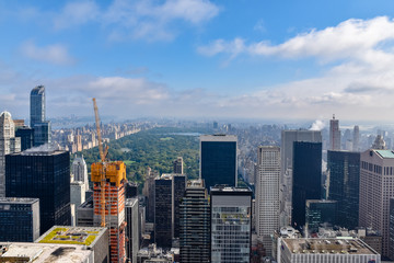 Fototapeta premium Aerial view of New York with skyscrapers, buildings in construction and central park in the background. Sunny day with some clouds. Concept of travel and construction. NYC, USA