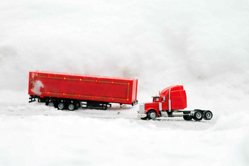 Festive truck in red. A toy car is standing with a detached cargo container. Side view. Against the background of snowdrifts. Winter. Christmas holidays.