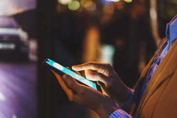 Cropped image of woman calling a taxi through the application on smartphone at night on city shopping street © fifeflyingfife