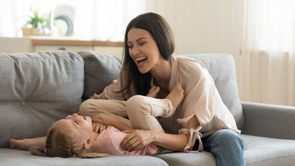 Obraz premium Cheerful mother tickling cute child daughter laughing playing on sofa