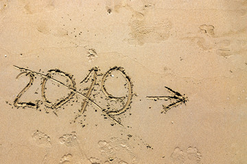 The inscription 2019 is painted with a finger on the sand and crossed out. Outgoing Year Concept. With arrow to the right