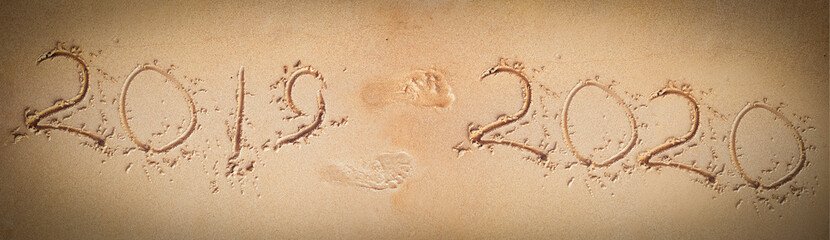 Concept. Sandy beach, the inscription 2019 from which footprints in the sand to the inscription 2020. The outgoing year. Happy New Year.