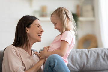 Laughing young mum tickling playing with kid daughter on couch