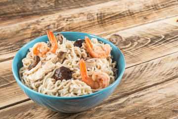 Chinese soup with udon noodles, pork, boiled eggs, mushrooms and prawns close-up in a bowl on the table