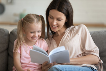 Caring mother and preschool child daughter reading book at home
