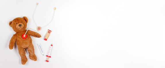 Teddy bear with toy stethoscope and toy medicine tools on white background. Top view. Copy space for text