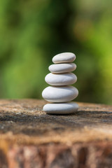Fototapeta na wymiar White stones cairn, poise light pebbles on wooden stump in front of green natural background, zen like, harmony and balance