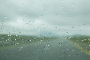 Rain drop on glass of the car road with fog or mist in green nature . Water drops on the glass in car . raindrops . water drops on glass background.
