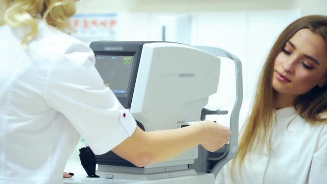 Beautiful woman checking her eyes in clinic. Refractometer tests human eyes and printing the results. Ophthalmologist examines female's eyes on modern device.