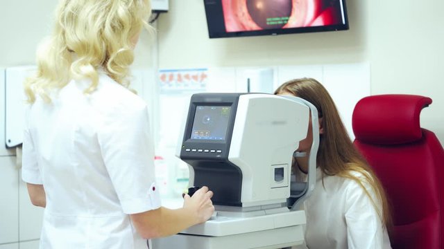 Doctor examining patient's eyes on modern device. Optometrist checks eyesight of a young woman with a refractometer in clinic.