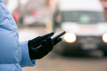 Girl holding a mobile phone in her hands while standing at a bus stop close up. Woman tracks the location of the bus using her smartphone online concept. © Natali