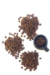  a clay cup filled with coffee beans next to three heaps of coffee beans on a white background. Flat lay