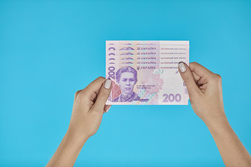 Female hands holding Ukrainian banknotes on blue background