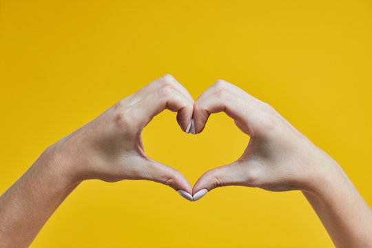 Beautiful female hands making heart sign on a yellow background