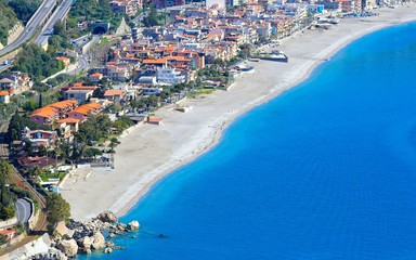 Clear sea, hotels and pebbly beach near Mazzeo Messina on east coast of island of Sicily, Italy.