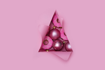 Xmas baubles pink color in triangular Torn hole and ripped of paper in a shape of Christmas tree. Christmas flat lay
