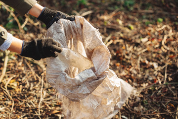 Eco activist  picking up dirty plastic bottles in park. Woman hand in glove picking up trash, collecting garbage in bag. Volunteer cleaning up nature from single use plastic