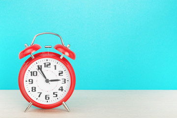 Red retro alarm clock with five minutes to three o'clock, on wooden table on a blue background. The concept of time, holiday, 5 minutes to the event, deadline. Layout with copy space for your text.