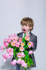 Surprised little boy with bouquet of tulips. Stylish little boy in elegant suit holds bouquet tulips. Gift to mum. Flower gift. Birthday, Women's Day, Mother's Day, Valentines day. Wedding concept.