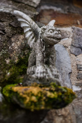 Gargoyle statue on stone building with moss