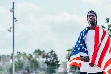 Serious African American man holding American flag on shoulder and looking away