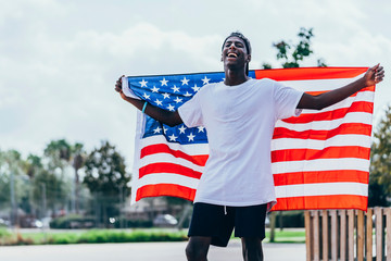 Serious African American man holding American flag on shoulder and looking away