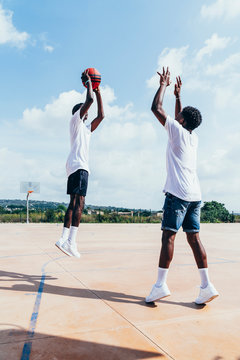 Side view of African American guys playing basketball in bright day on play ground