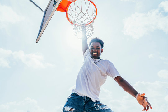 Powerful energetic African American sportsman hanging on basketball lap after scoring ball in net on playground