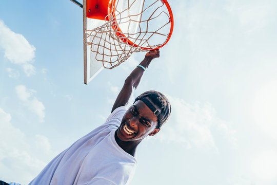 Powerful energetic African American sportsman hanging on basketball lap after scoring ball in net on playground