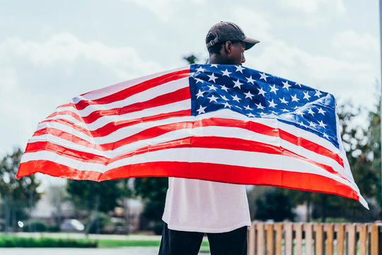 Serious African American man holding American flag on shoulder and looking away