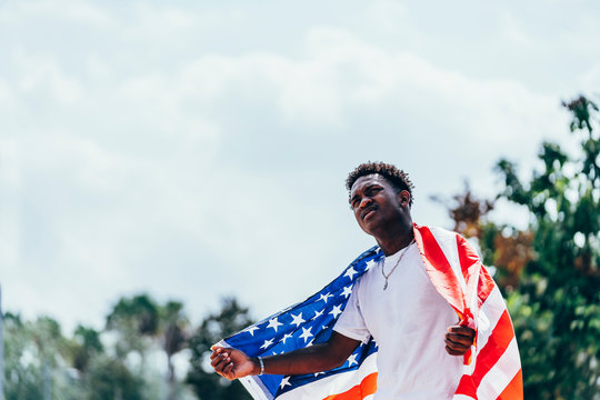 Serious African American man holding American flag on shoulder and looking away