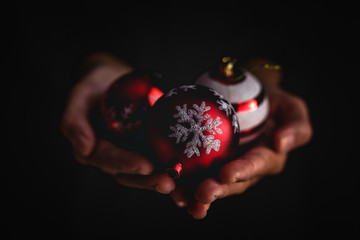 Closeup anonymous person demonstrating handful of decorated Christmas balls against black background