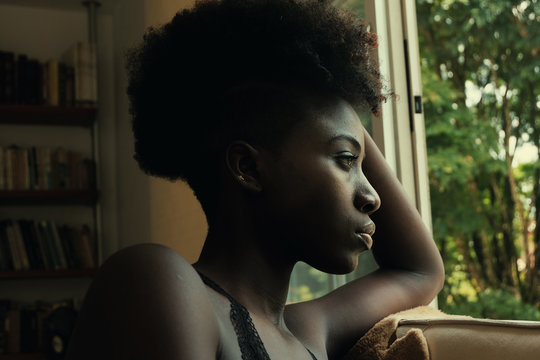 Side view of African American mysterious disappointed resentful sad woman looking out windows
