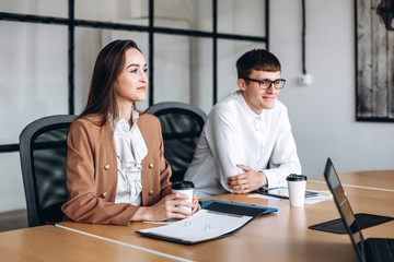 Attractive brunette drinking coffee, her glasses colleague listens attentively to the meeting.