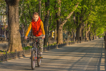 A boy of 8 years old in an orange vest rides a bicycle in a city park on a sunny spring morning. © Виктор Кеталь
