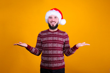Fototapeta na wymiar Studio portrait of handsome bearded man wearing christmas sweater with snowflake ornament and Santa hat, posing over the yellow wall, copy space. Festive background. Male with facial hair smiling.