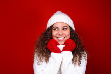 Studio portrait of young woman with dark skin and long curly hair wearing knitted turtle neck sweater over the festive red wall with a lot of copy space for text. Close up, isolated background.