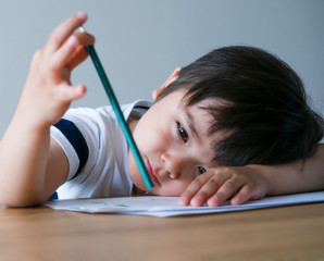 Candid shot of Kid boy holding colour pencil sitting alone with bored face, Preschool child boy laying head down on table with deep in throught, Five years old kid bored with school homework