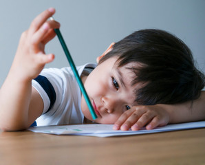 Candid shot of Kid boy holding colour pencil sitting alone with bored face, Preschool child boy...