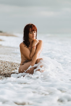 Young nude free calm female posing with closed eyes while sitting in a rocky beach